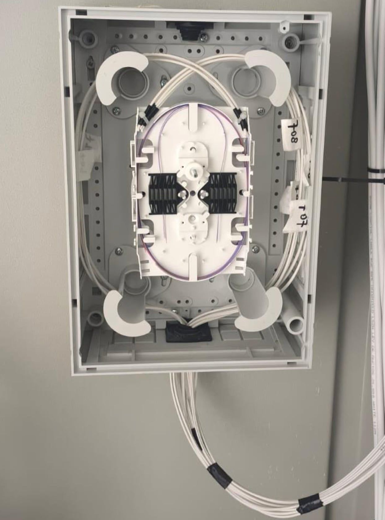 Caja de fibra óptica abierta, con la bandeja de empalmes por fusión y los cables rotulados con el departamento de destino
