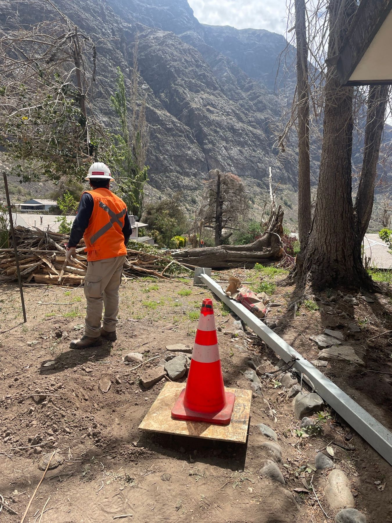 Trabajador con casco y chaleco reflectante junto a una cámara de paso señalizada con un cono, durante la canalización en el campamento