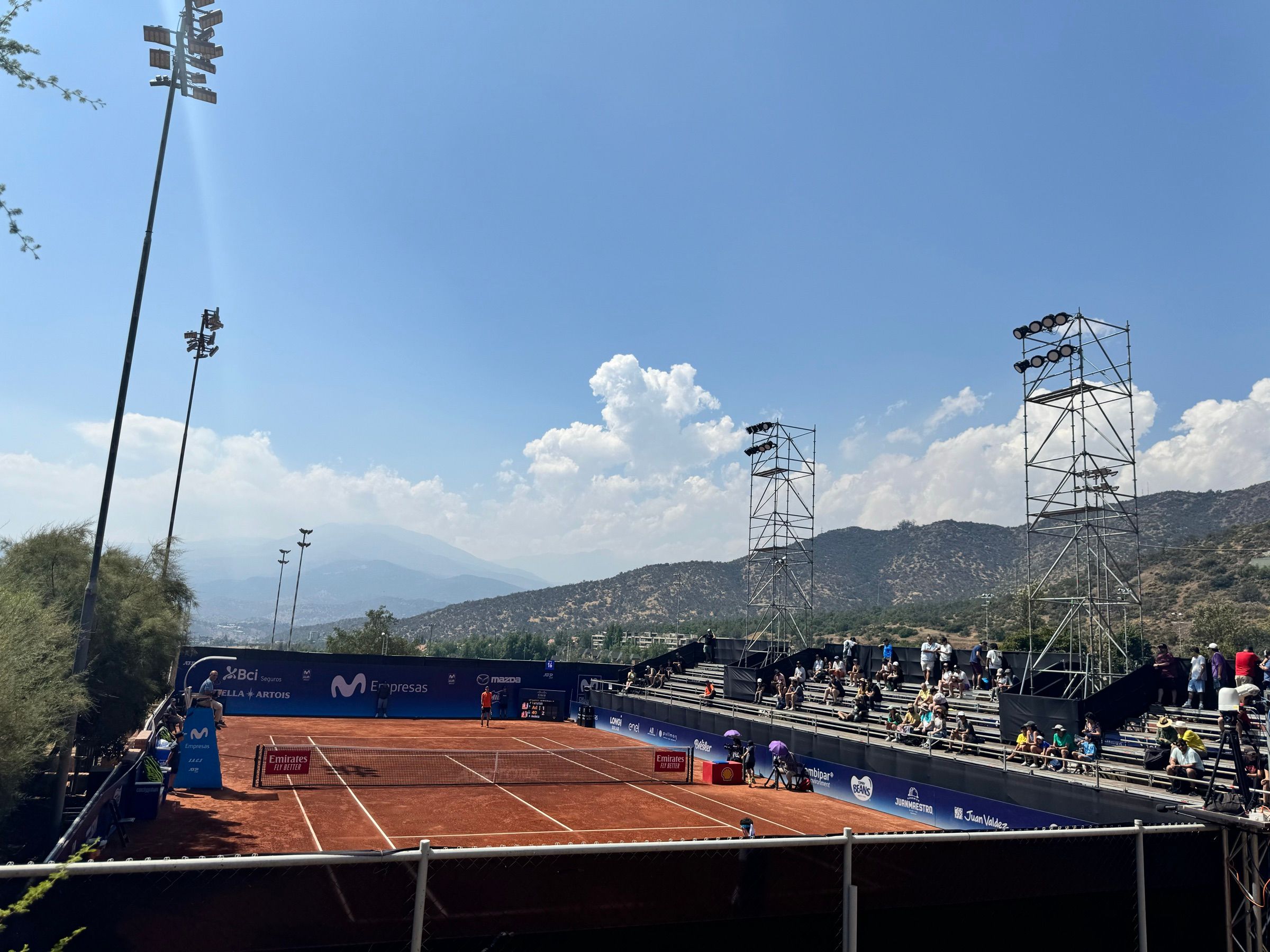 Cancha central de arcilla del torneo con público en las tribunas, torres de iluminación y el cerro de fondo