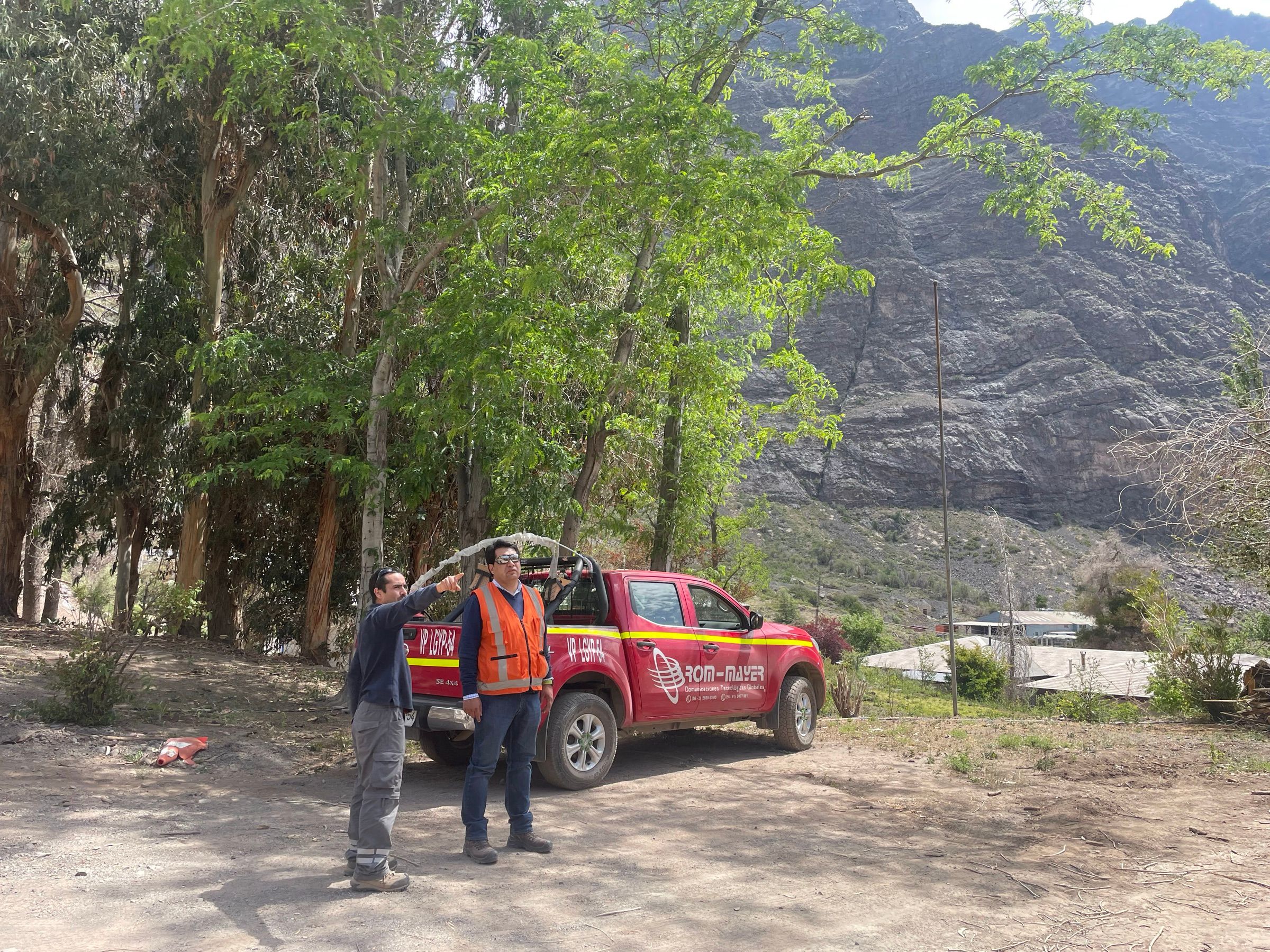 Dos profesionales de Rom Mayer junto a una camioneta de la empresa en el campamento, con la ladera del cerro de fondo