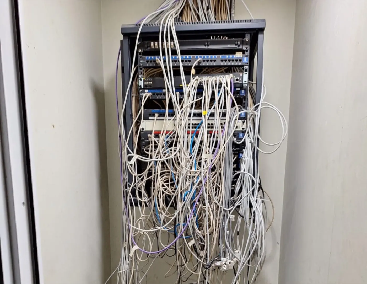 Rack de comunicaciones con el cableado enredado y patch cords colgando fuera de los organizadores