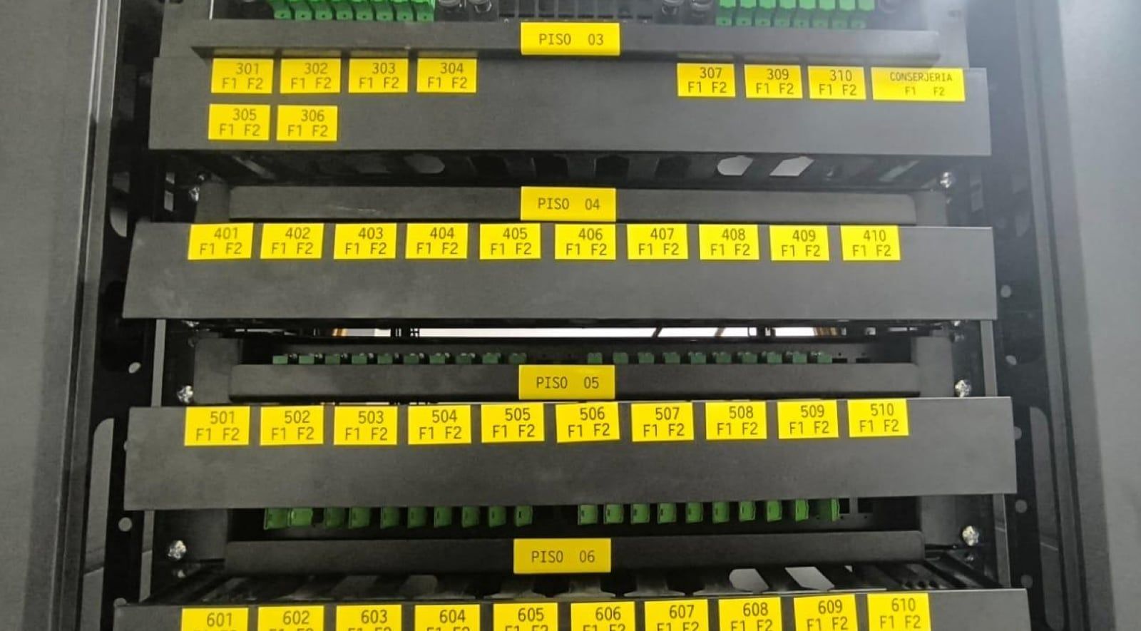 Rack de fibra óptica en la sala de telecomunicaciones del edificio, con cada puerto rotulado en amarillo con el número de departamento y agrupado por piso