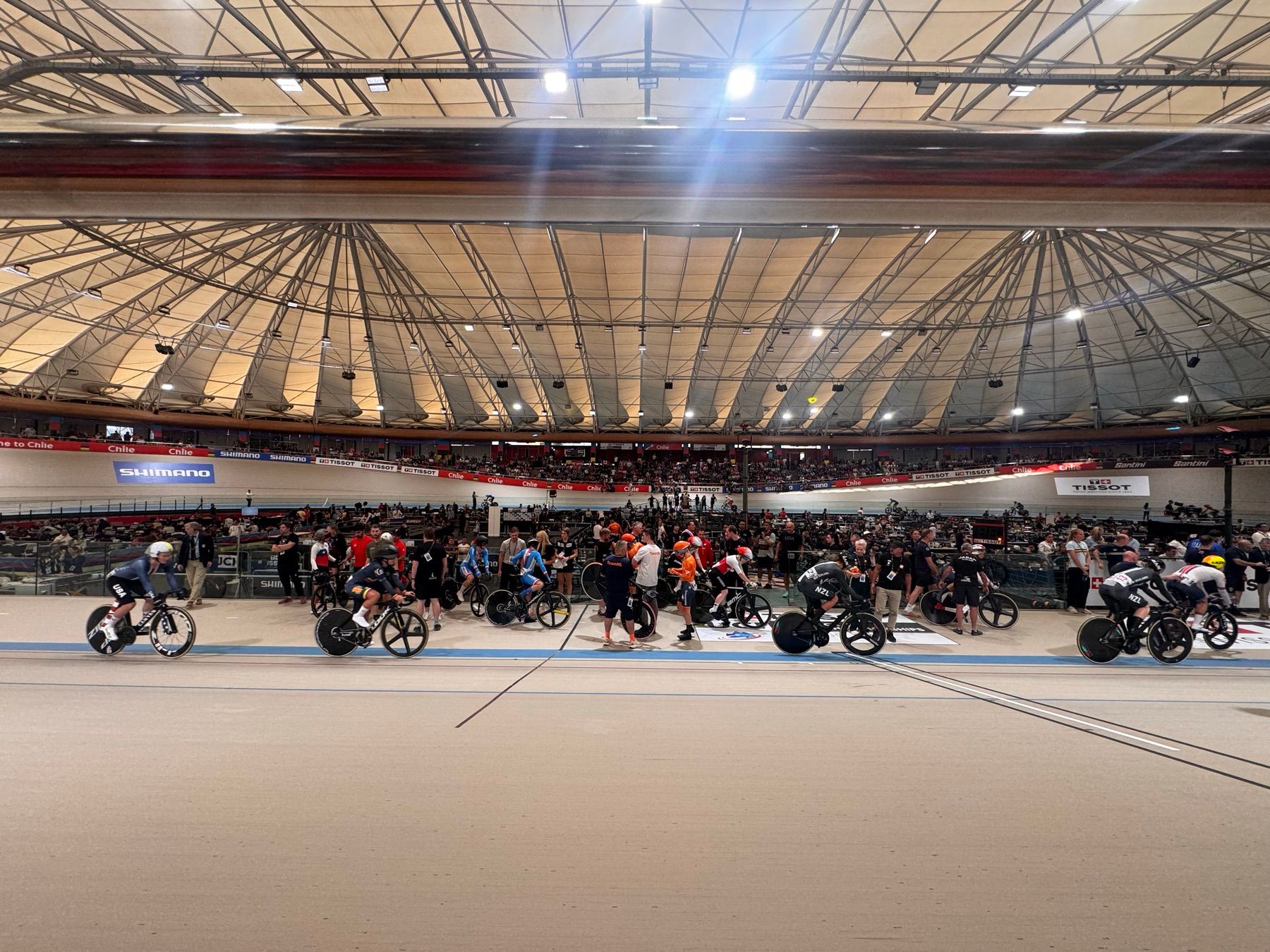 Pista del velódromo durante la competencia, con ciclistas en carrera y las tribunas llenas
